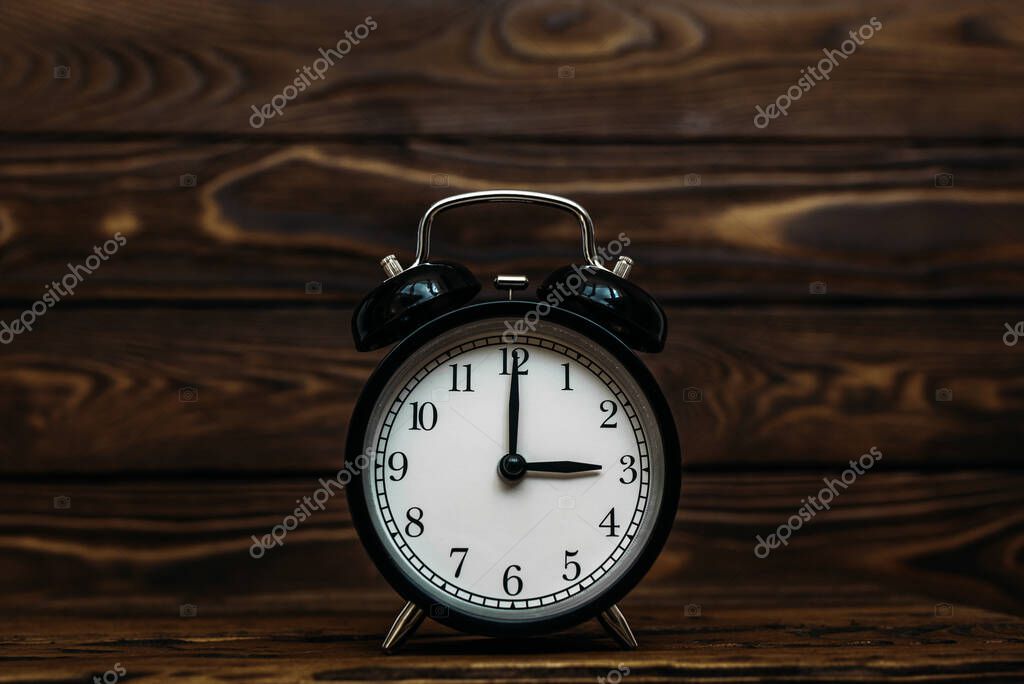Clock on a wooden background. The clock shows the time of three o'clock in the afternoon. The clock shows the time of three o'clock in the morning. An image of a retro clock showing 03:00 pm/am. Copy space