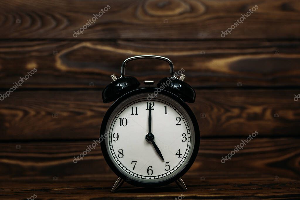 Clock on a wooden background. The clock shows the time of five o'clock in the afternoon. Clock showing the time of five o'clock in the morning. An image of a retro clock showing 05:00 pm/am. Copy space