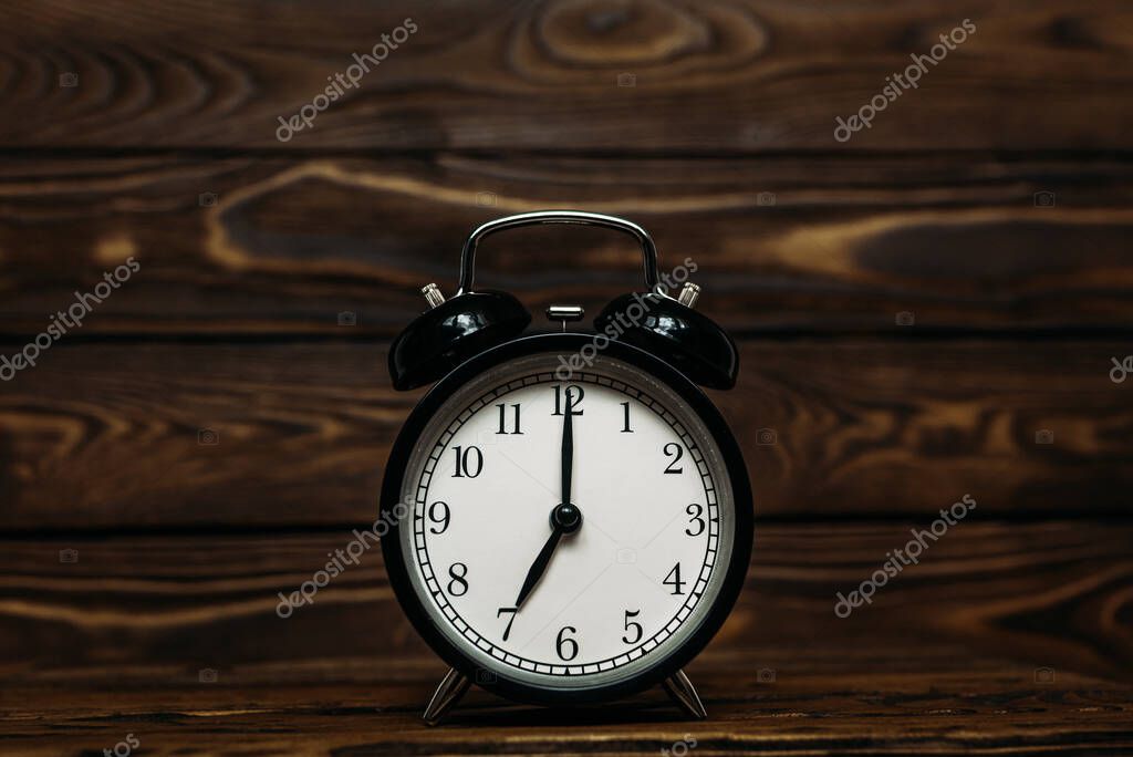Clock on a wooden background. The clock shows the time of seven o'clock in the afternoon. The clock shows the time seven o'clock in the morning. An image of a retro clock showing 07:00 pm/am. Copy space