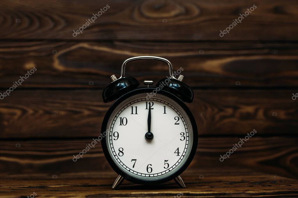 Clock on a wooden background. The clock shows the time of twelve o'clock in the afternoon. Clock showing the time of twelve o'clock in the morning. An image of a retro clock showing 12:00 pm/am. Copy space