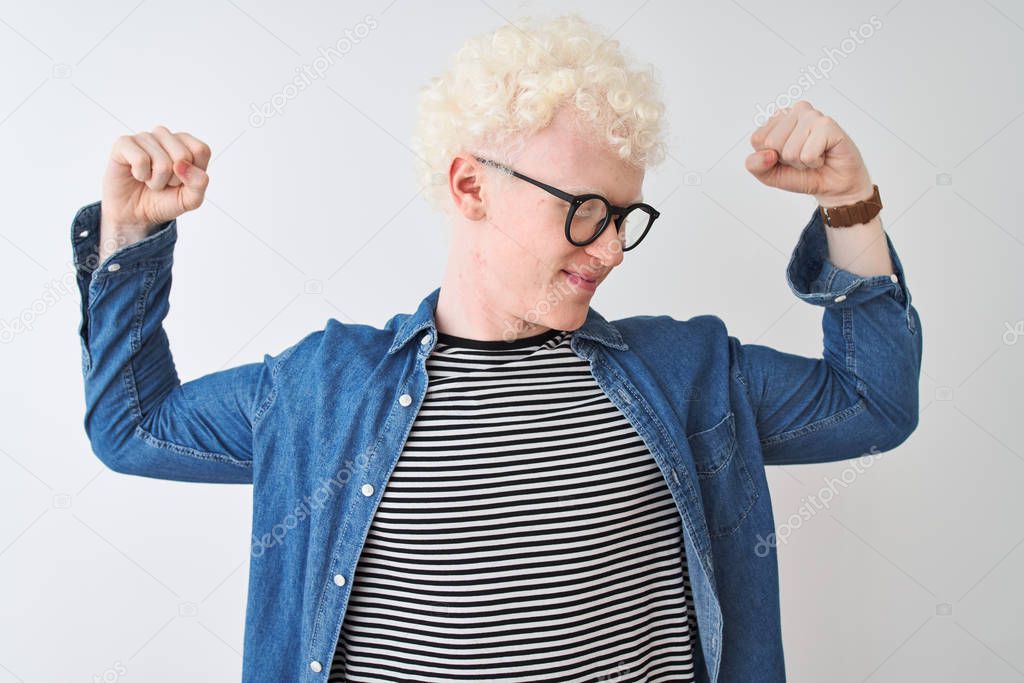 Young albino blond man wearing denim shirt and glasses over isolated white background showing arms muscles smiling proud. Fitness concept. model released