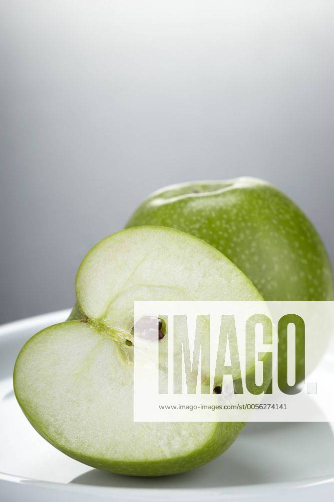 Zwei grüne Granny Smith Äpfel, ein ganzer und ein halber, auf einem weißen Teller iblmjh02076504