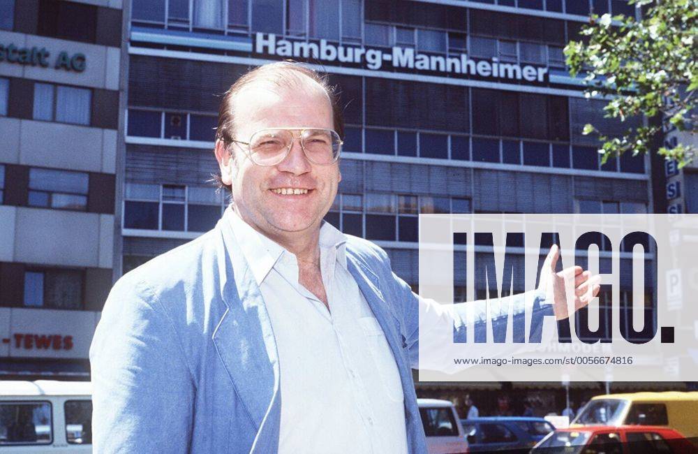 Günter Geiermann 07 87 rag quer halb draußen lächelnd Gebäude Mann Fernsehen Schauspiel Werbung Brille Halbglatze dunkelhaarig Hamburg-Mannheimer Logo zeigend