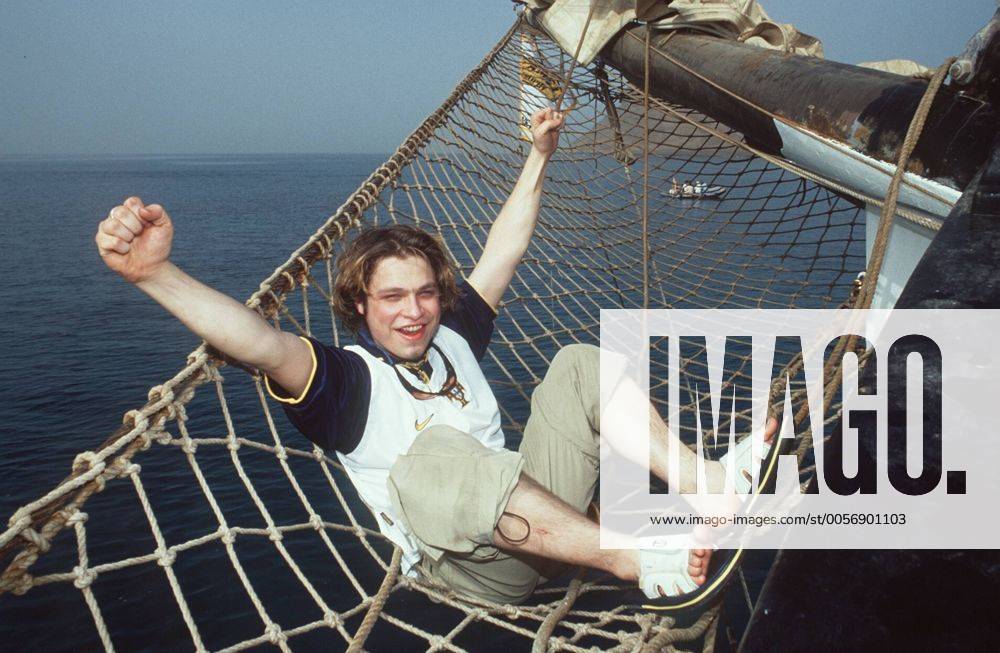 Tim Sander (Schauspieler) bei der Camel Trophy (Kapverdische Inseln) 03 00 mapo Mann geboren am 27.07.1978 in Berlin Sprecher Synchronsprecher Synchronsprechen Synchronisation Synchron Schauspiel TV Fernsehen Serie GZSZ Gute Zeiten, schlechte Zeiten RTL Rolle des Kai Scholl dunkelhaarig kurzhaarig Bart Bärtchen Ziegenbart Schmuck Ring leger T-Shirt bunt Hose beige Shorts Bermudas liegend draussen in Netz Hängematte befestigt an Boot Segelboot Schiff Segelschiff von aussen über dem Wasser an der Aussenwand ganz quer lächelnd posierend Arme ausgebreitet ausbreitend Fototermin Camel Trophy im März 2000 auf den Kapverdischen Inseln