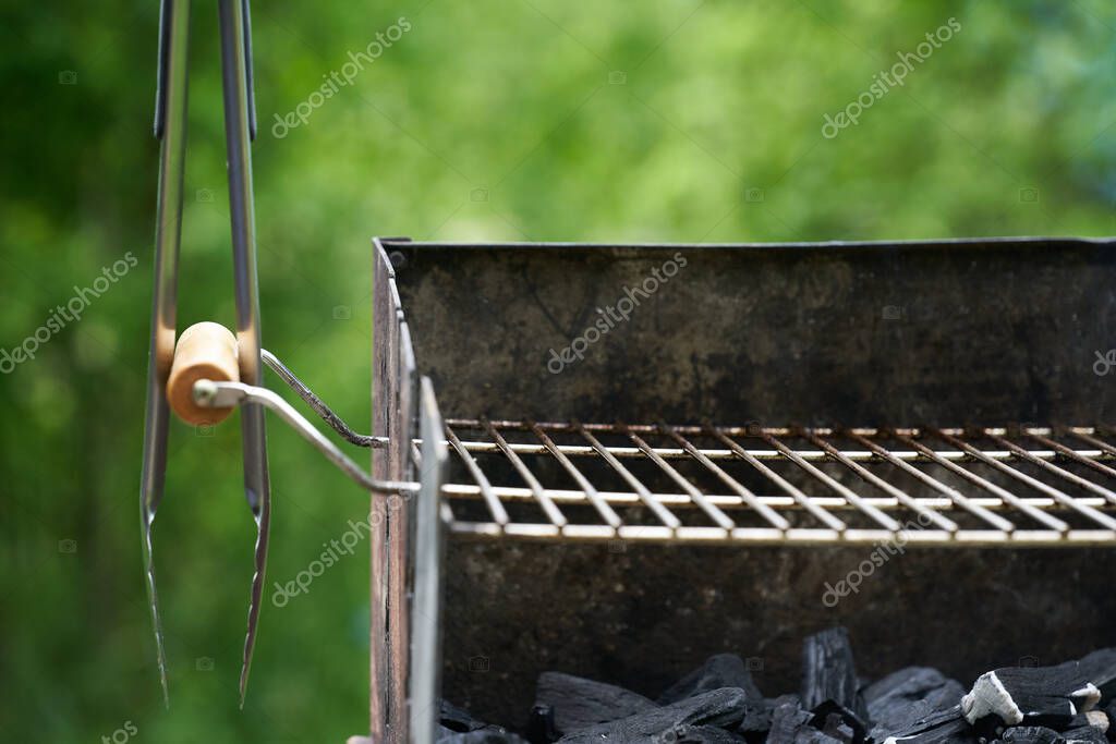 Barbecue tongs (Grillzange) on a wooden handle from a charcoal grill with dirty rust. Green nature in the background.