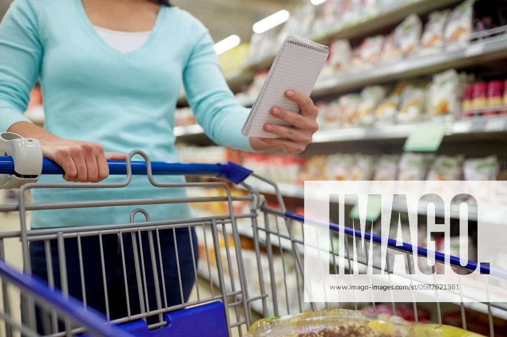 Consumerism and people concept - woman with notebook and shopping cart or trolley buying food at grocery store or supermarket. woman with food in shopping cart at supermarket ,model released, Symbolfoto; Konsumismus und Personen Konzept Frau mit Notizbuch und Einkaufen Karren Oder Rollwagen kaufend Lebensmittel im grocery Ladengeschaeft Oder Supermarkt Frau mit Lebensmittel in Einkaufen Karren im Supermarkt ,model released, Symbolfoto ING_33594_207964