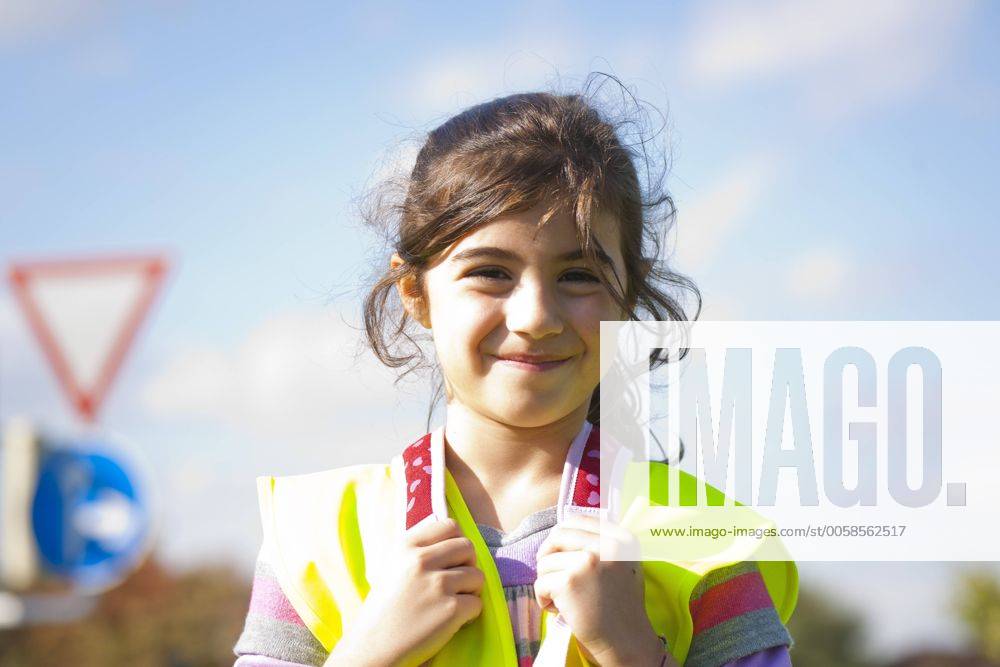 IMAGO Creative: Gesellschaft, Schule, Schulanfang kleines Mädchen mit Schulranzen und Warnweste vor einem Verkehrsschild