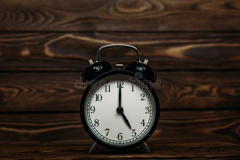 Clock on a wooden background. The clock shows the time of five o`clock in the afternoon. Clock showing the time of five o`clock, Clock on a wooden background. The clock shows the time of five o`clock in the afternoon. Clock showing the time of five o`clock in the morning. An image of a retro clock showing 05:00 pm/am. Copy space