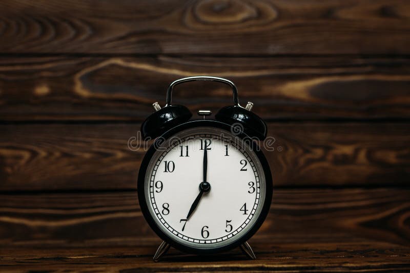 Clock on a wooden background. The clock shows the time of seven o`clock in the afternoon. The clock shows the time seven o`clock, Clock on a wooden background. The clock shows the time of seven o`clock in the afternoon. The clock shows the time seven o`clock in the morning. An image of a retro clock showing 07:00 pm/am. Copy space