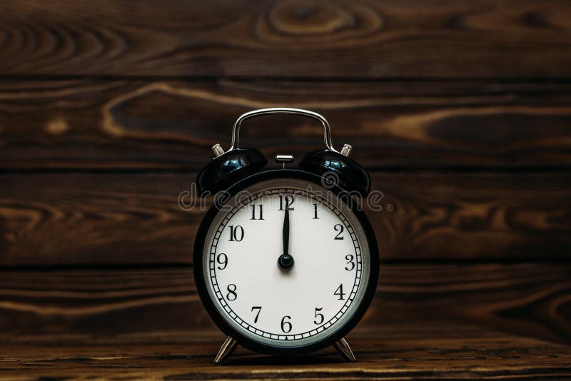 Clock on a wooden background. The clock shows the time of twelve o`clock in the afternoon. Clock showing the time of twelve o`, Clock on a wooden background. The clock shows the time of twelve o`clock in the afternoon. Clock showing the time of twelve o`clock in the morning. An image of a retro clock showing 12:00 pm/am. Copy space