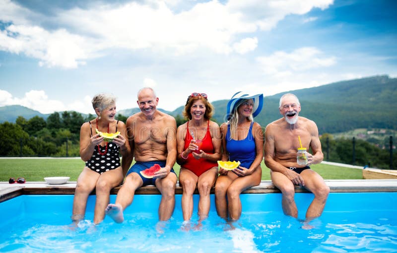 Group of cheerful seniors sitting by swimming pool outdoors in backyard., Group of cheerful seniors sitting by swimming pool outdoors in backyard, having fun.