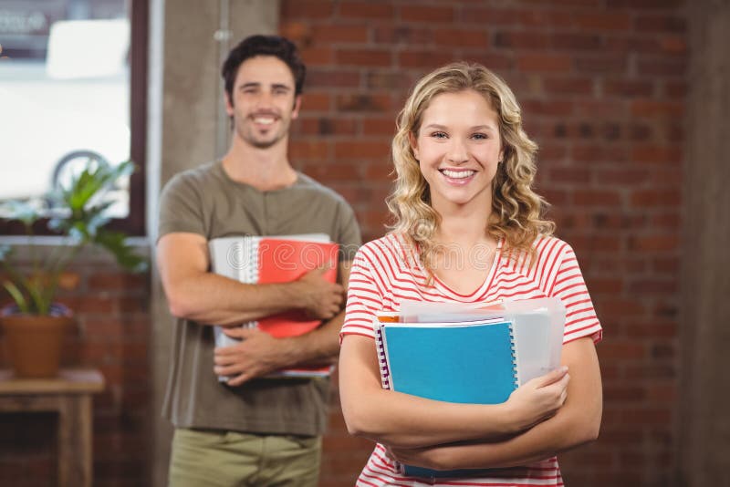 Portrait of smiling businesswoman holding files and folders in office, Portrait of smiling businesswoman holding files and folders while standing in creative office