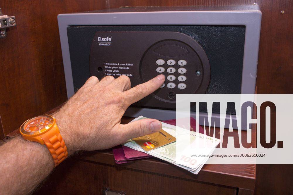 Person tippt eine Zahlenkombination in einen geschlossenen Tresor, davor eine Kreditkarte, Reisepässe und Bargeld, in einem Hotelzimmer iblmmx04060843