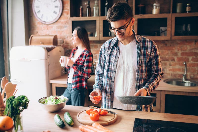 Husband hugs wife while she cooking fresh salad, Husband hugs wife while she cooking fresh vegetable salad in bowl on the kitchen. Diet food preparation. Couple prepares romantic dinner, healthy lifestyle