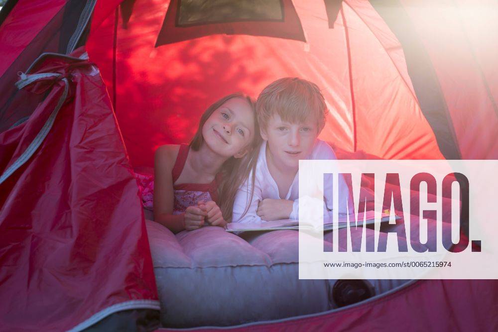 Portrait of brother and sister lying in a red tent with a book model released Symbolfoto SARF001931