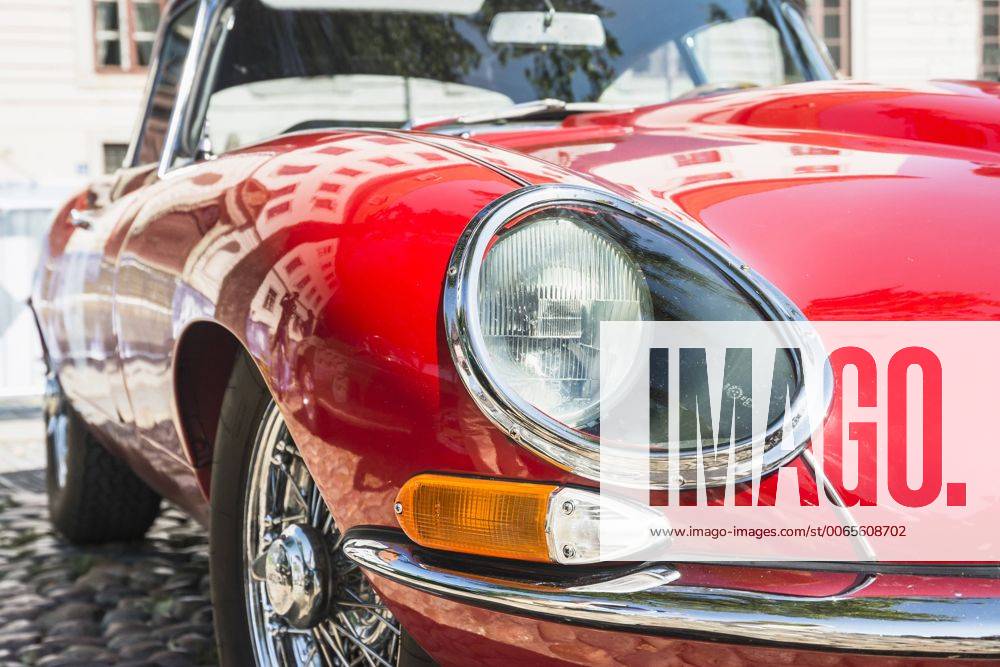Detail eines Jaguar E-Type Baujahr 1964 in rot, Frontpartie mit Scheinwerfer, Blinker, Speichenrad und Motorhaube, Spiegelungen auf dem glänzenden Lack von Kotflügel und Kühlerhaube Sinnliche Formen