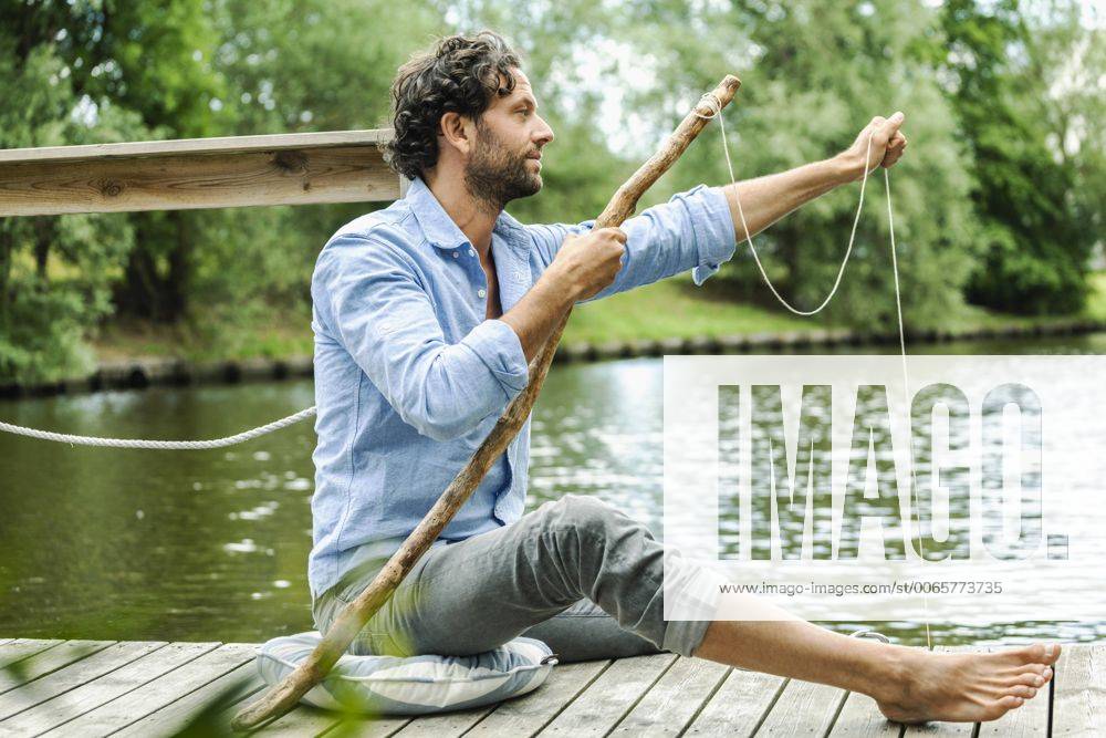 Man sitting on platform at the waterside with selfmade fishing rod model released Symbolfoto property released FMKF001962