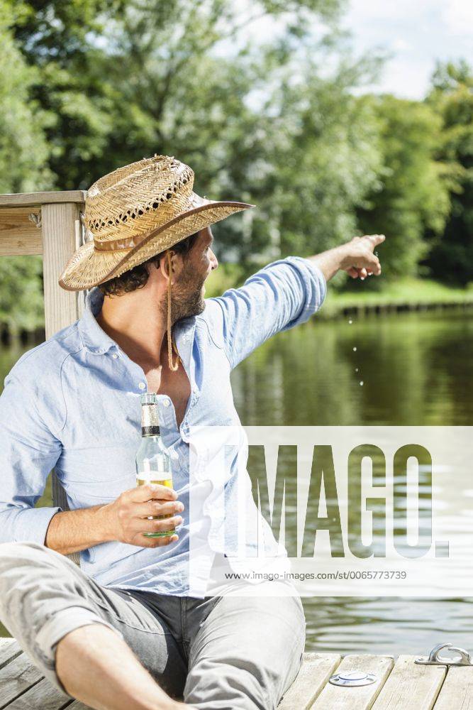 Man sitting on platform at the waterside with beer bottle pointing his finger model released Symbolfoto property released FMKF001966