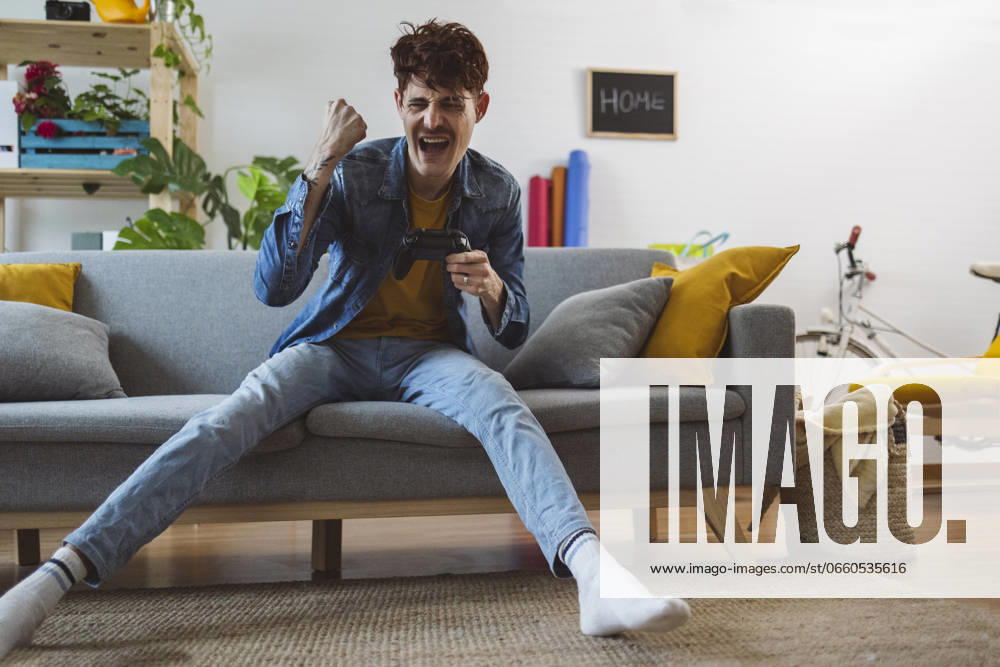 IMAGO Creative, Lifestyle, Gaming Cheerful man winning video game with controller at home model released, Symbolfoto property released, ALZF00282