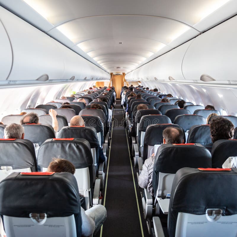 Interior of commercial airplane with passengers on their seats during flight., Interior of commercial airplane with unrecognizable passengers on their seats during flight shot from the rear of airplane.