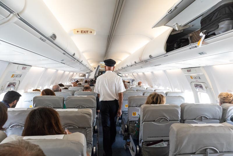 Interior of commercial airplane with passengers on their seats during flight., Interior of commercial airplane with unrecognizable passengers on their seats during flight. Steward in blue white uniform walking the aisle of commercial airplane.