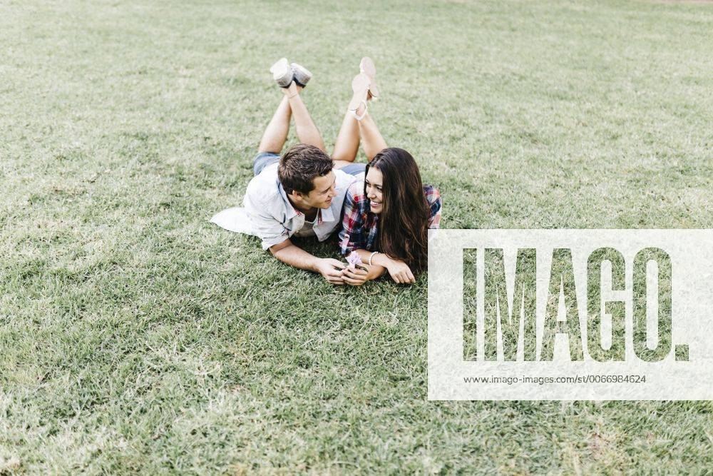 Young couple in love lying on a meadow in a park looking at each other JRFF000112