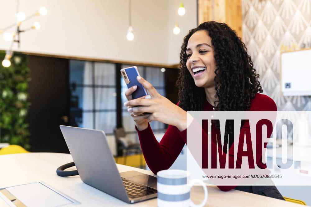 Happy businesswoman surfing net through smart phone at desk in office model released, Symbolfoto property released, WPEF08848