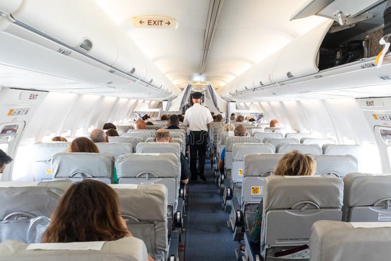 Interior of commercial airplane with passengers on their seats during flight., Interior of commercial airplane with unrecognizable passengers on their seats during flight. Steward in blue white uniform walking the aisle of commercial airplane.