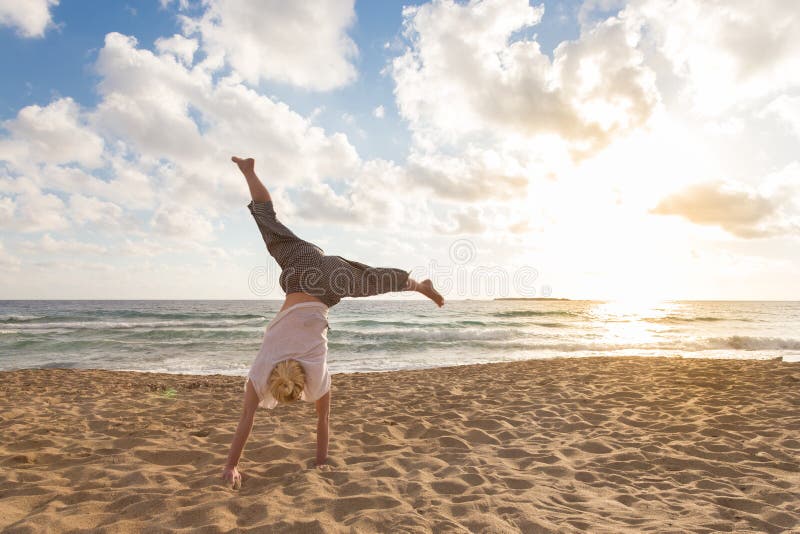 Free Happy Woman Turning Cartwheel Enjoying Sunset on Sandy Beach., Relaxed woman enjoying sun, freedom and life turning cartwheel on beautiful beach in sunset. Young lady feeling free, relaxed and happy. Vacations, freedom, happiness, enjoyment and well being. model released