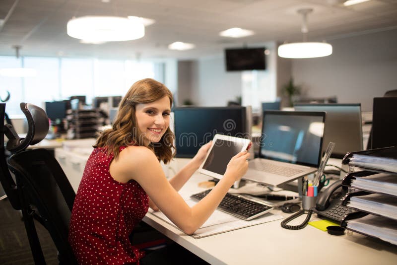 Portrait of smiling businesswoman holding digital tablet in office, Portrait of smiling businesswoman holding digital tablet while sitting at office desk model released
