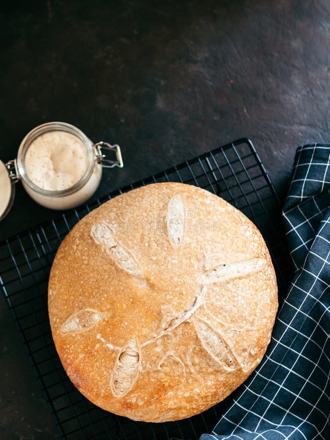 Wheat round sourdough bread, copy space, top view, Wheat round sourdough bread and sourdoug starter in glass jar. Top view of delicious homemade sourdough bread on black background with copy space. Home made sourdough bread making concept. Vertical.