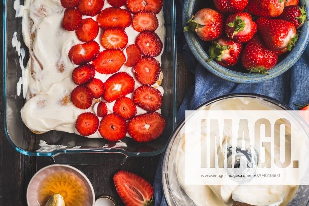Strawberry dessert making. Dish with sliced berries and cream on dark rustic background, top view ,model released, Symbolfoto