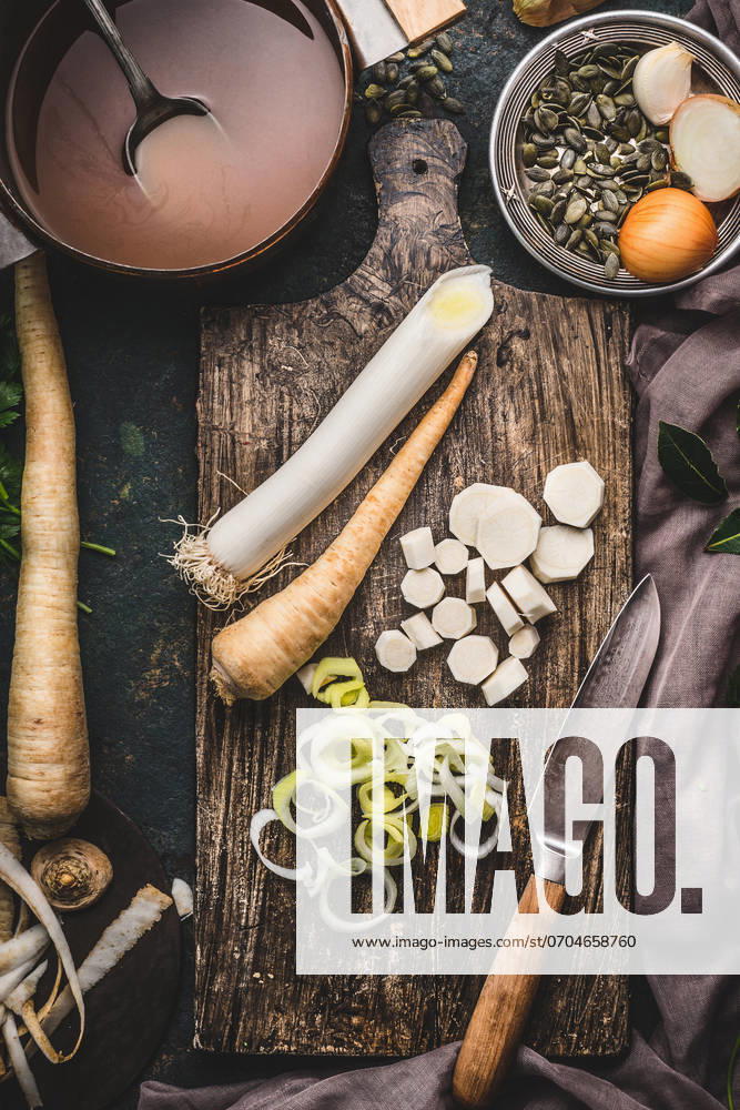 Healthy vegetables cooking and eating concept. Leek and parsnip root vegetables on cutting board with knife and pot with broth on dark rustic background, top view. ,model released, Symbolfoto