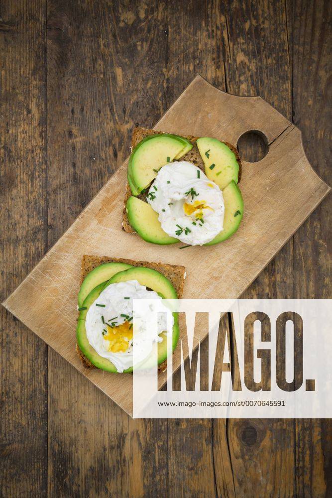 Wholemeal bread slices with sliced avocado and poached eggs on wooden board LVF004669