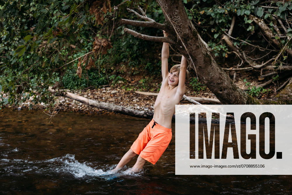 IMAGO Creative, Jahreszeit Sommer, Sommerferien Smiling child swinging on tree branch over river during summer Glenallen, Missouri, United States CR_WEKW240709-1474545-01 ,model released, Symbolfoto