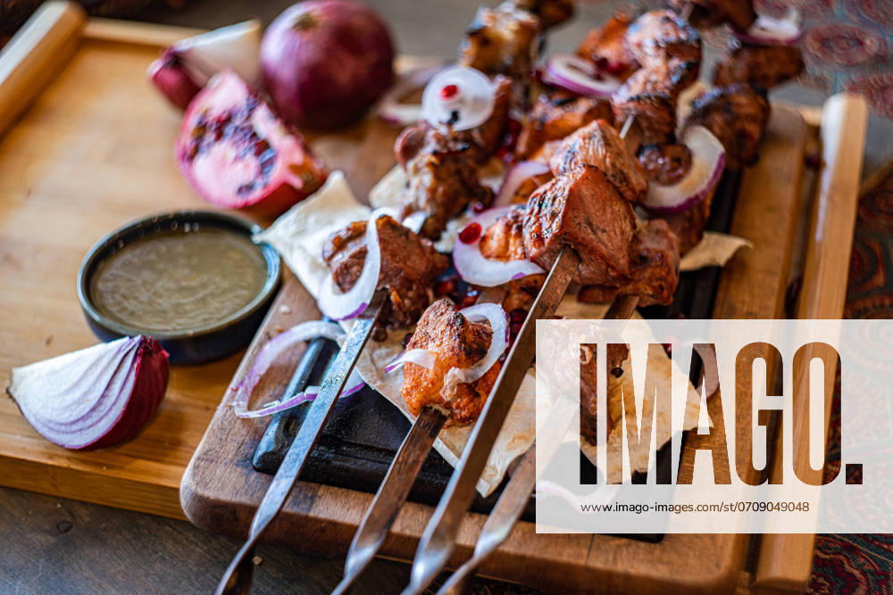 A rustic presentation of Georgian mtsvadi, showcasing succulent grilled meat skewers, served on a wooden board with sliced onions, pomegranate seeds, and traditional flat bread Perfect for culinary themes Model Released AnnaBogush_ID22661_660722_004