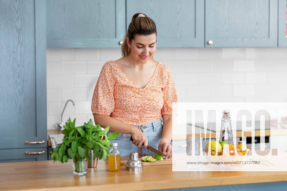 Culinary and people concept - happy smiling young woman making cocktail drinks with lime and peppermint at home kitchen. woman making cocktail drinks at home kitchen ,model released, Symbolfoto