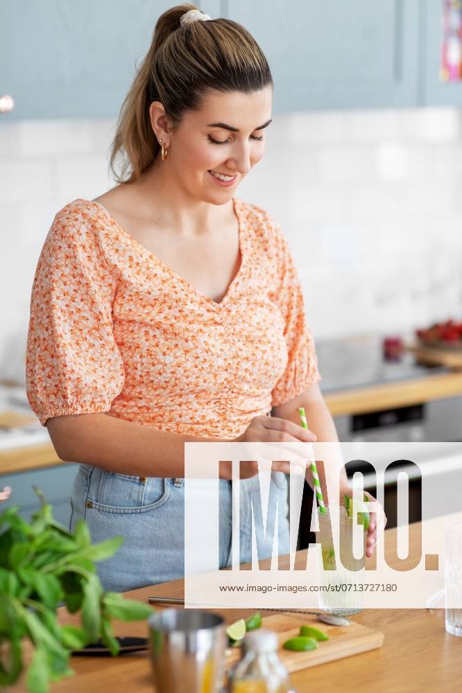 Culinary and people concept - happy smiling young woman making cocktail drinks with lime and peppermint at home kitchen. woman making cocktail drinks at home kitchen ,model released, Symbolfoto