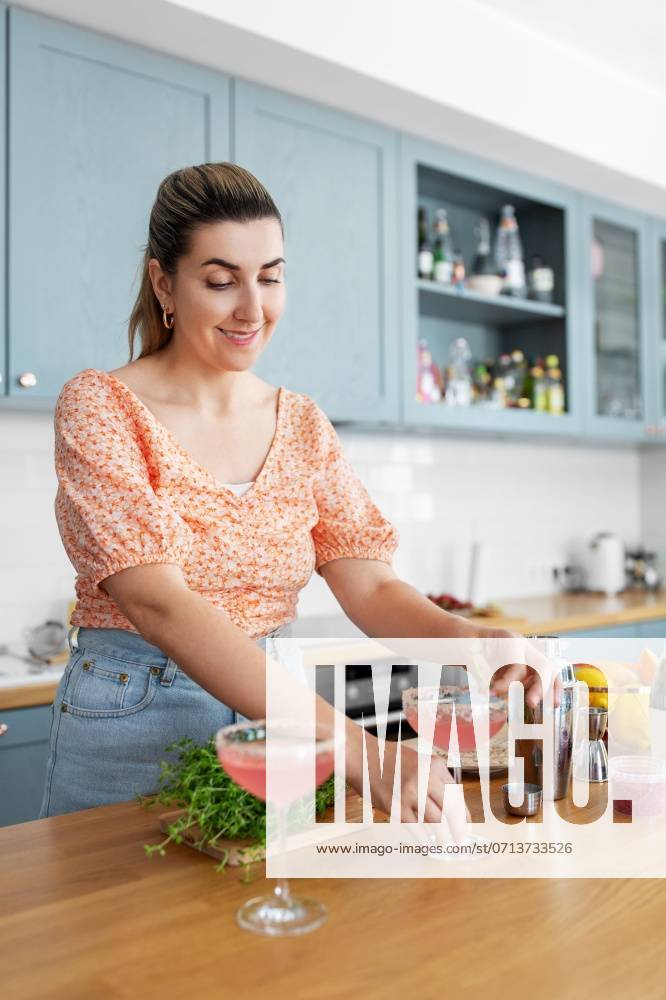 Culinary and people concept - happy smiling young woman making cocktail drinks at home kitchen. woman making cocktail drinks at home kitchen ,model released, Symbolfoto