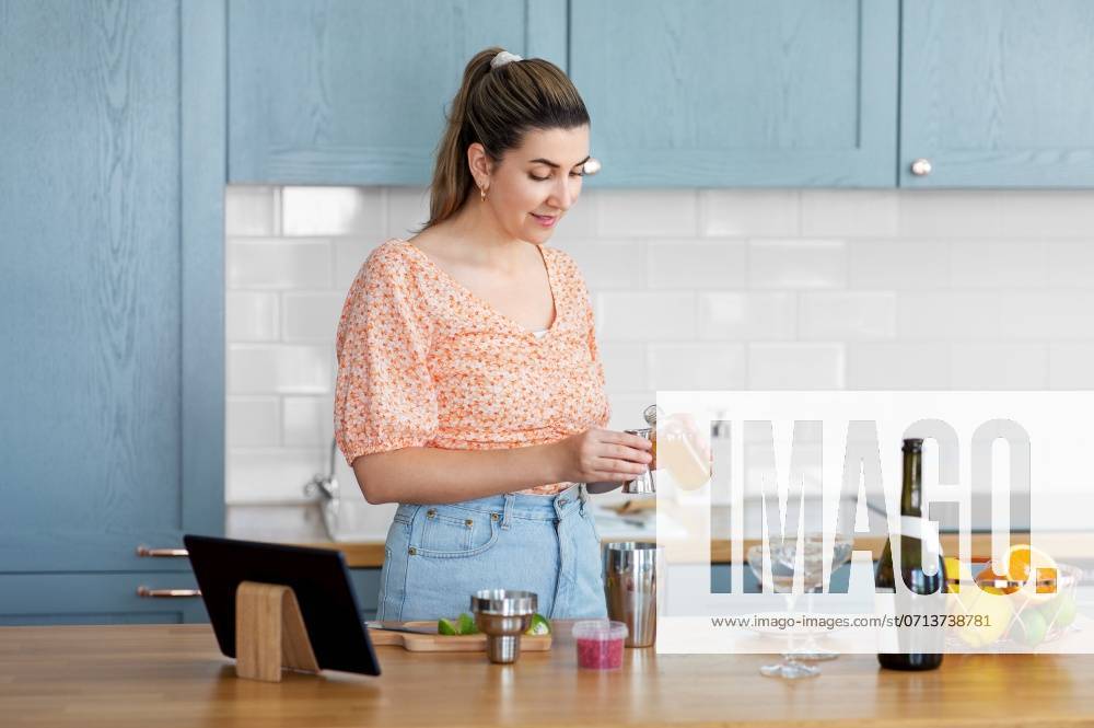 Culinary and people concept - happy smiling young woman with tablet pc computer making cocktail drinks at home kitchen. woman with tablet pc making cocktails at kitchen ,model released, Symbolfoto