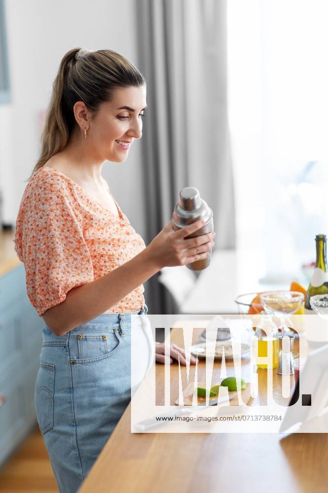 Culinary and people concept - happy smiling young woman with tablet pc computer making cocktail drinks at home kitchen. woman with tablet pc making cocktails at kitchen ,model released, Symbolfoto