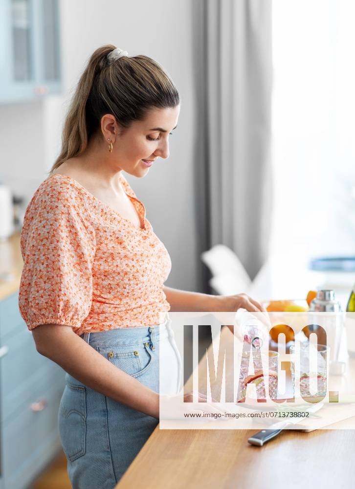 Culinary and people concept - happy smiling young woman making cocktail drinks at home kitchen. woman making cocktail drinks at home kitchen ,model released, Symbolfoto