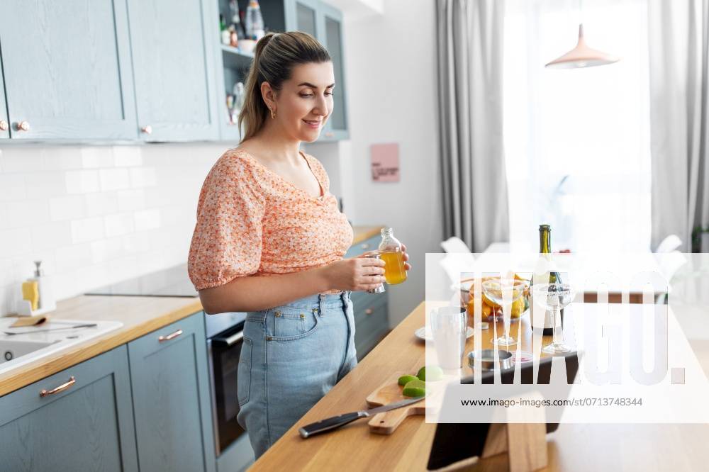 Culinary and people concept - happy smiling young woman with tablet pc computer making cocktail drinks at home kitchen. woman with tablet pc making cocktails at kitchen ,model released, Symbolfoto