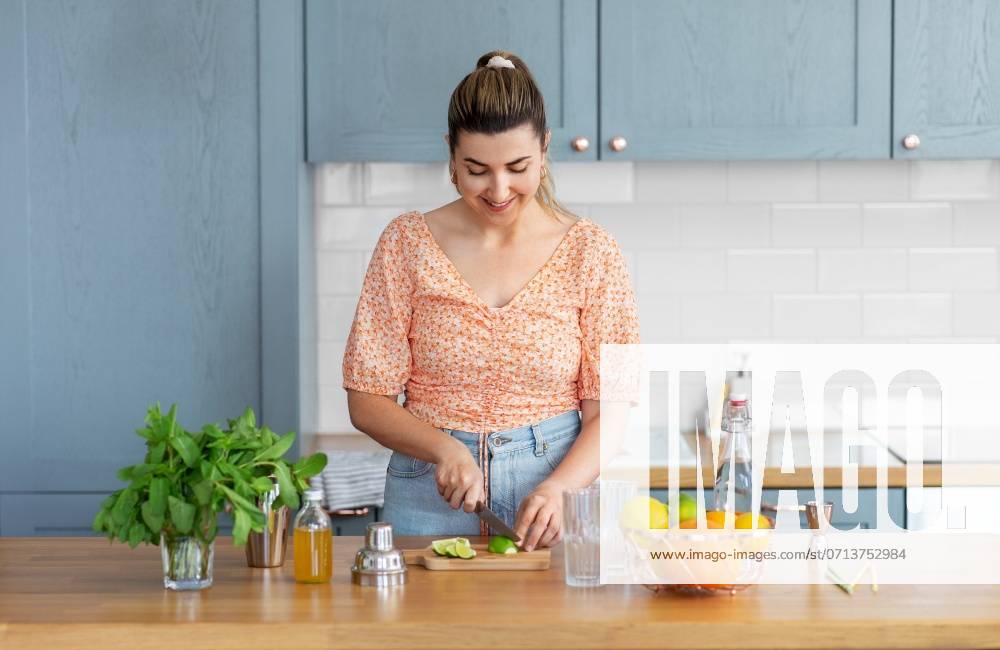 Culinary and people concept - happy smiling young woman making cocktail drinks with lime and peppermint at home kitchen. woman making cocktail drinks at home kitchen ,model released, Symbolfoto