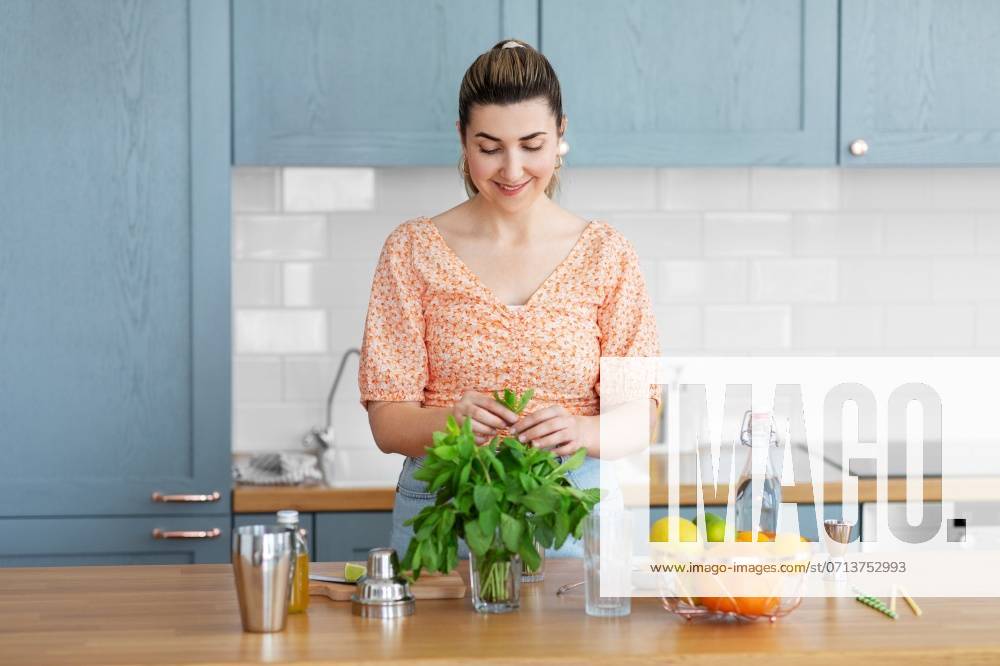 Culinary and people concept - happy smiling young woman making cocktail drinks with lime and peppermint at home kitchen. woman making cocktail drinks at home kitchen ,model released, Symbolfoto