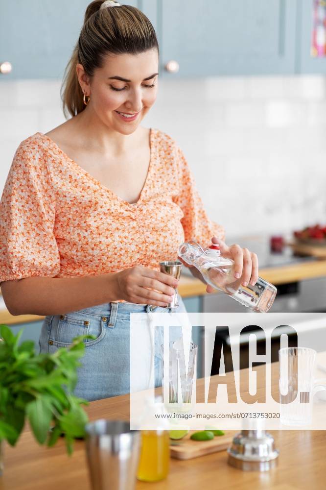 Culinary and people concept - happy smiling young woman making cocktail drinks at home kitchen. woman making cocktail drinks at home kitchen ,model released, Symbolfoto