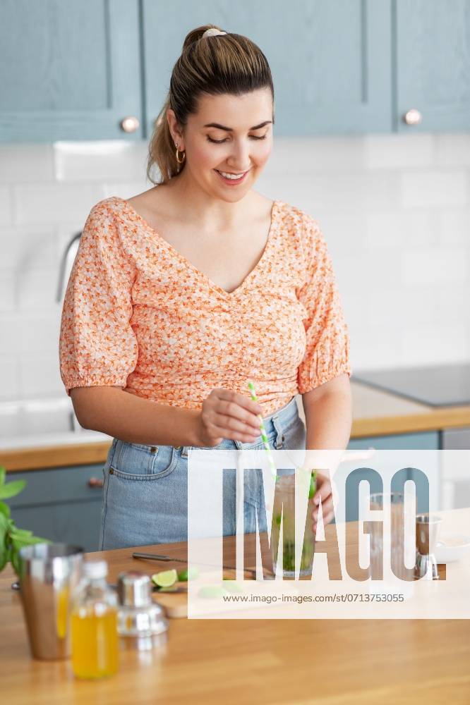 Culinary and people concept - happy smiling young woman making cocktail drinks with lime and peppermint at home kitchen. woman making cocktail drinks at home kitchen ,model released, Symbolfoto