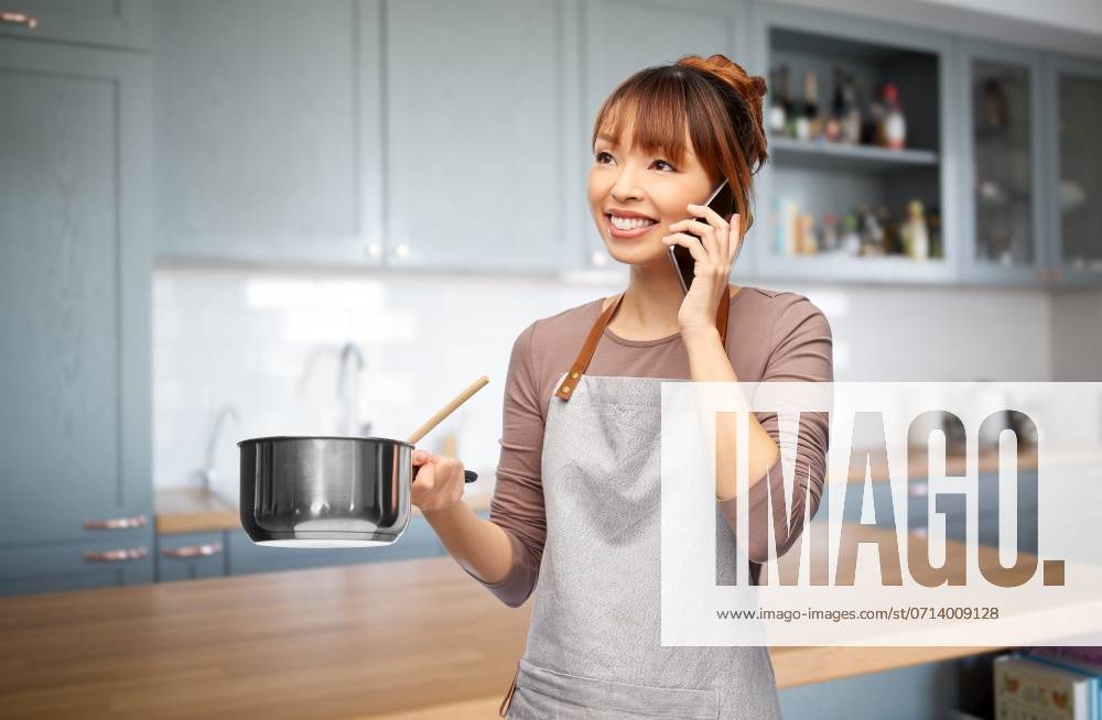 Culinary and people concept - happy smiling woman in apron with saucepan cooking food and calling on smartphone over kitchen background. happy female chef with saucepan calling on phone ,model released, Symbolfoto