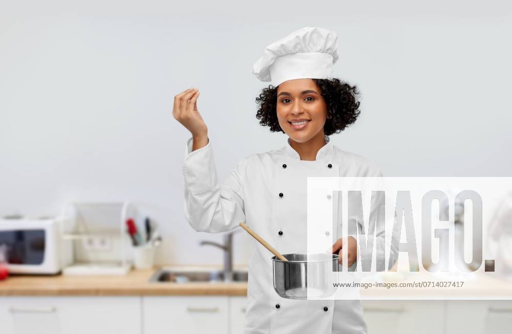 Culinary and people concept - happy smiling female chef in toque with saucepan cooking food showing gourmet sign over kitchen background. female chef with saucepan and spoon cooking food ,model released, Symbolfoto