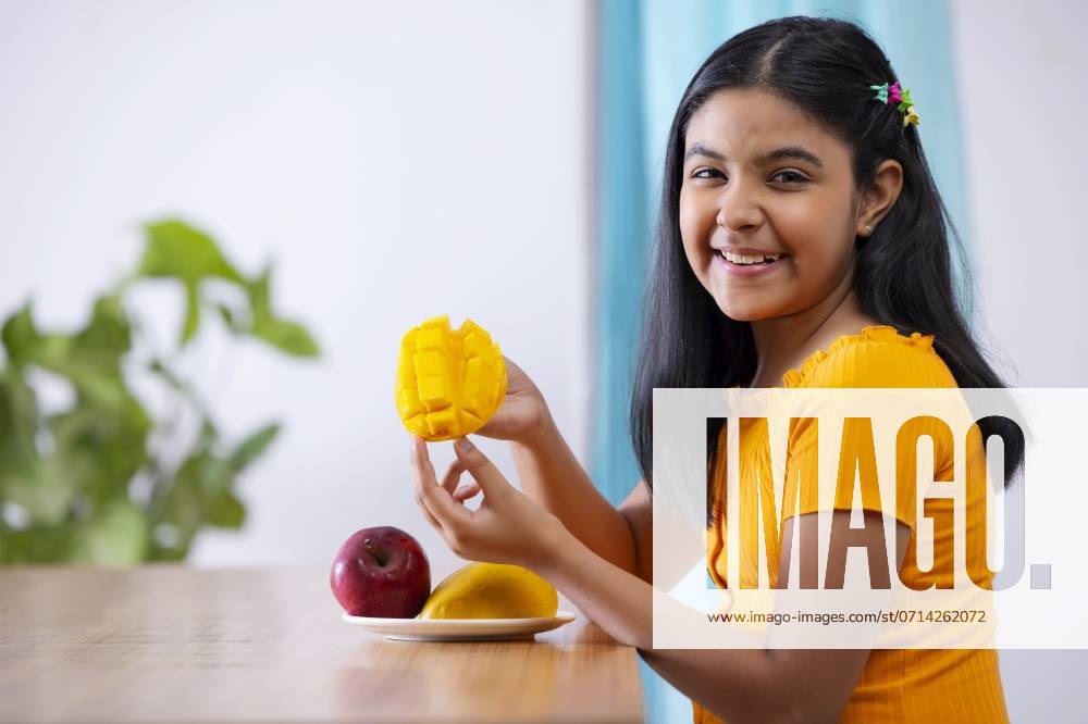 Portrait of cheerful girl holding a segmented slice of mango ,model released, Symbolfoto